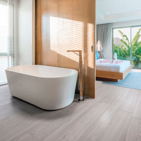 Eine weiße freistehende Badewanne steht auf hellem Holzboden neben einer Holztrennwand und bietet Blick auf ein Schlafzimmer mit Eine weiße freistehende Badewanne steht auf hellem Holzboden neben einer Holztrennwand und bietet Blick auf ein Schlafzimmer mit