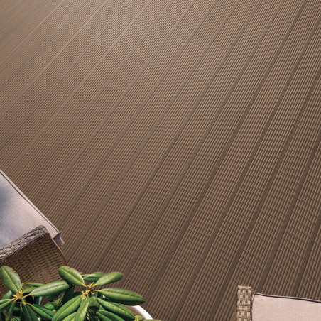 Brown tile with parallel grooves lies outdoors beside wicker chair and green plant, creating a patterned, textured flooring surf
