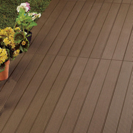 Des carreaux marron nervurés forment un patio. bordé d'herbe verte et de fleurs en pot colorées ajoutant un contraste décoratif 