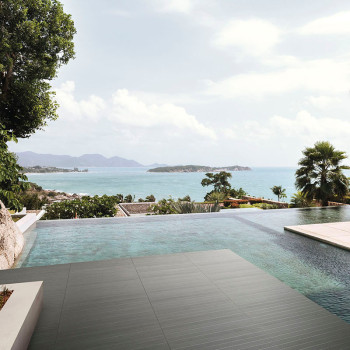 Ein moderner Infinity-Pool erstreckt sich nahtlos zu einem ruhigen Meer, umgeben von üppigem Grün und fernen Inseln unter klarem