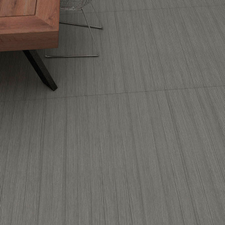 Una pata de mesa de madera descansa sobre azulejos texturizados de color gris con sutiles líneas verticales, ubicada en un ambie