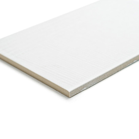 Un carreau rectangulaire, fin et blanc repose sur une surface homogène, mettant en valeur sa texture lisse et ses bords légèreme