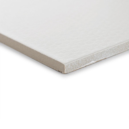 Un azulejo blanco con una superficie texturizada sutil se encuentra sobre una superficie plana, mostrando su grosor y borde liso