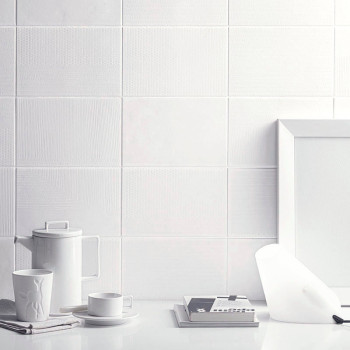 Los azulejos de cerámica blanca componen una pared texturizada, acompañada de una configuración minimalista de una tetera, una t