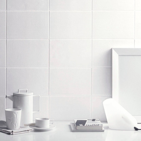 Los azulejos de cerámica blanca componen una pared texturizada, acompañada de una configuración minimalista de una tetera, una t