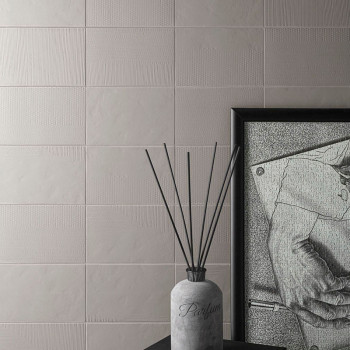 Un frasco de perfume del que sobresalen finas varillas se encuentra sobre una superficie oscura, junto a un dibujo monocromático