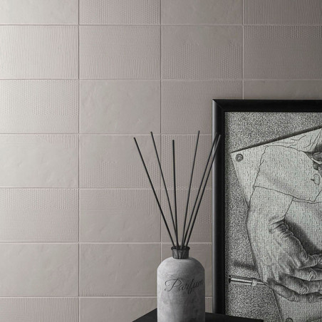 Eine Parfümflasche mit herausstehenden dünnen Stäbchen steht auf einer dunklen Oberfläche neben einer gerahmten monochromen Zeic