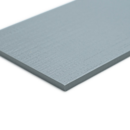 Un carreau de céramique rectangulaire bleu grisâtre repose à plat, présentant une subtile texture hachurée, sur un fond blanc.