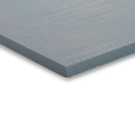 Un carreau gris lisse et rectangulaire avec une fine texture de motif de grille repose sur une surface plane et blanche, vue dep