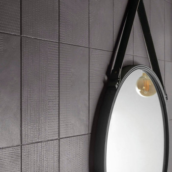 Un mur carrelé texturé gris foncé reflète un miroir circulaire avec une sangle qui le suspend, capturant la lueur chaude des amp