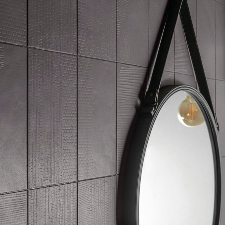 Un mur carrelé texturé gris foncé reflète un miroir circulaire avec une sangle qui le suspend, capturant la lueur chaude des amp