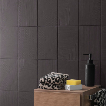 Azulejos de textura oscura cubren una pared. Sobre una superficie de madera, toallas con estampado de leopardo descansan junto a