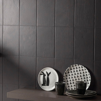 Azulejos escuros e texturizados formam uma parede moderna. Pratos com desenhos minimalistas de coelho e triângulo ficam em uma p