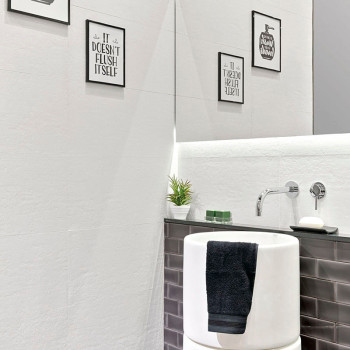 Een moderne badkamer is voorzien van een witte wastafel versierd met een zwarte handdoek, omgeven door ingelijste berichten met 