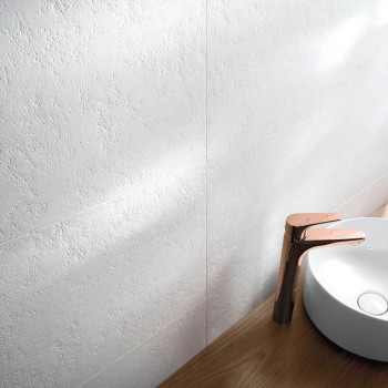 Un carrelage mural texturé blanc est doucement éclairé, à côté d'un élégant comptoir en bois avec un lavabo rond blanc et un rob