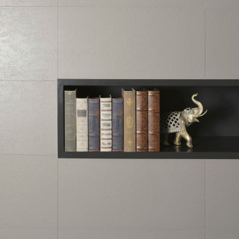 A recessed black shelf holds six vertically stacked books and a decorative silver elephant figurine, set against a gray tiled wa