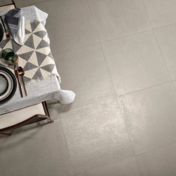Beige tegels vormen een gladde, naadloze vloer en reflecteren het licht. Aangrenzend staat een eettafel met een kleed met geomet