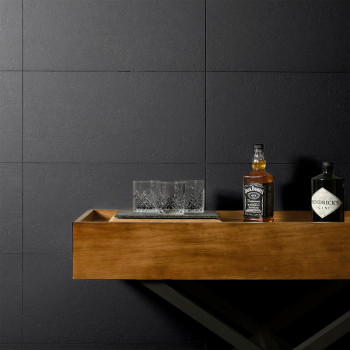 A wooden table holds two liquor bottles, Jack Daniels and Hendricks Gin, and a crystal glass against a dark tiled wall.