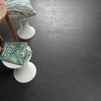 Dark gray, textured floor tiles lie in a grid pattern. Cushioned stools with green leaf-patterned pillows are placed nearby in a