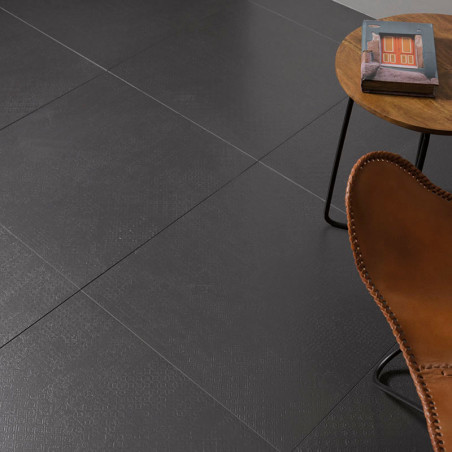 Les carreaux carrés gris foncé forment un sol lisse. Une chaise en cuir marron se trouve près d’une table d’appoint ronde en boi