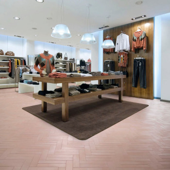 Een houten tafel toont opgevouwen kleding op een bruin tapijt in een moderne winkel, omgeven door hangende kleding en zachte ver