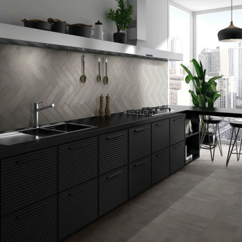 Cozinha moderna com bancadas pretas e armários alinhados contra uma parede de azulejos claros em espinha. A luz do sol entra atr