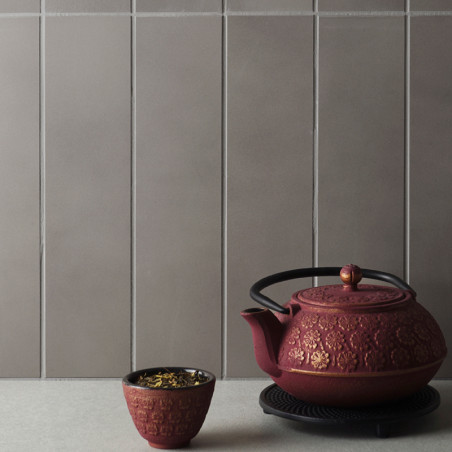 A textured, maroon teapot with a decorative pattern sits on a trivet beside a matching teacup filled with loose tea. Behind, ver