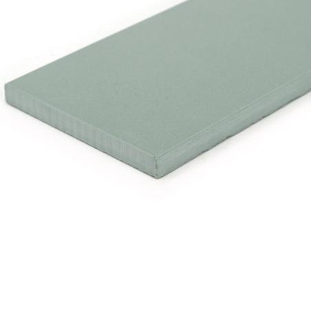 Un azulejo plana, rectangular, de color verde claro yace sobre una superficie blanca, mostrando su superficie lisa y su espesor 