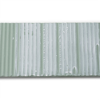 Un azulejo texturizado rectangular presenta ranuras verticales y un tono verde pálido con un texto tenue: `CUMEL CA 45 HELITOMBO