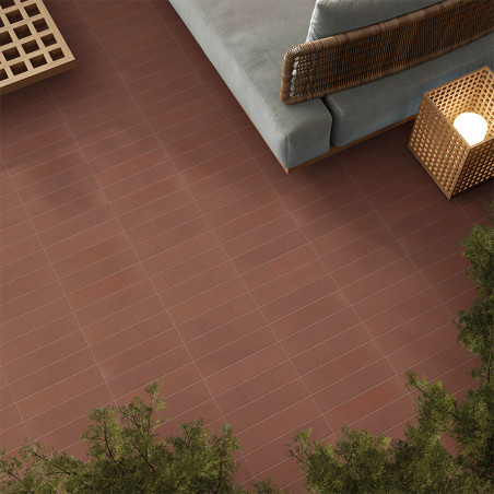 Des carreaux marron recouvrent le sol, bordé de plantes vertes. Un panier en osier avec une lumière et un canapé rembourré se tr