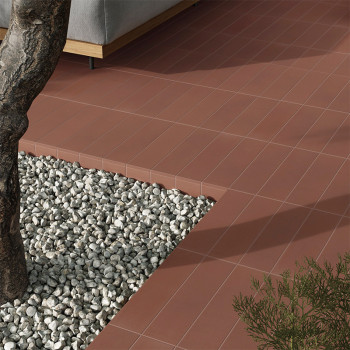 Les carreaux de terre cuite forment une surface de patio propre adjacente à une zone de gravier avec un tronc d'arbre. Un canapé