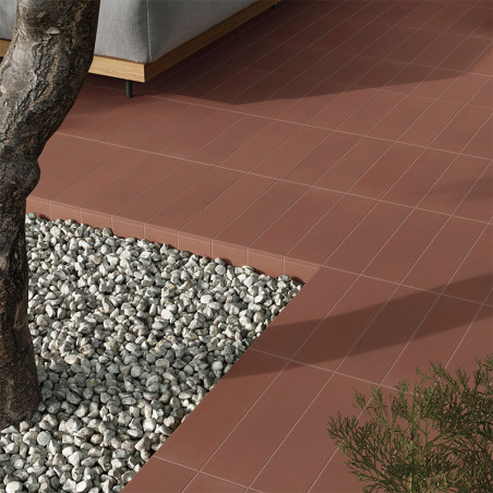 Les carreaux de terre cuite forment une surface de patio propre adjacente à une zone de gravier avec un tronc d'arbre. Un canapé