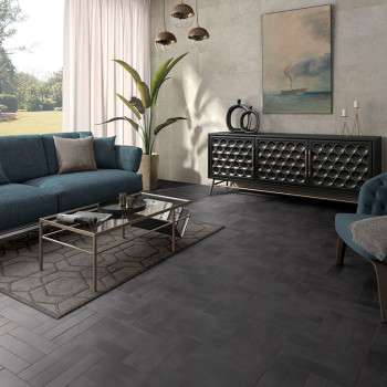 Un azulejo gris con diseño de espiga cubre el piso de la sala, rodeado por un sofá azul, una mesa de café de vidrio y arte abstr