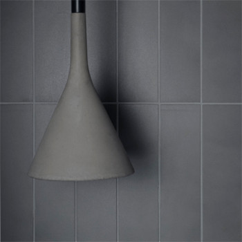 Un luminaire en forme de cône est suspendu sur fond de carreaux gris lisses et rectangulaires, créant une esthétique minimaliste