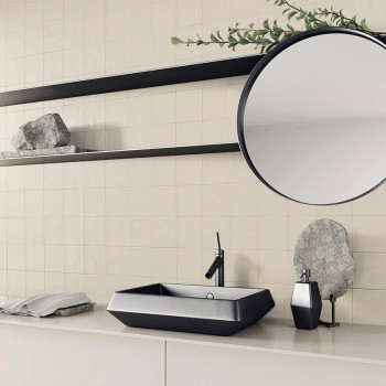 Un évier noir au design épuré est monté sur un comptoir beige minimaliste. Au-dessus, un miroir rond et des étagères contiennent