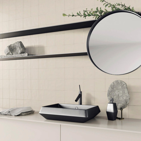 Uma pia preta com design elegante é montada em uma bancada bege minimalista. Acima, um espelho redondo e prateleiras com pedras 