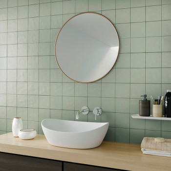 Un lavabo ovalado blanco se encuentra sobre una encimera de madera debajo de un gran espejo redondo, rodeado de azulejos verdes,