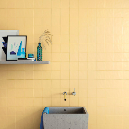 Una pared de azulejos de color amarillo mate presenta un lavabo de concreto minimalista con una toalla azul, ubicado debajo de u Una pared de azulejos de color amarillo mate presenta un lavabo de concreto minimalista con una toalla azul, ubicado debajo de u