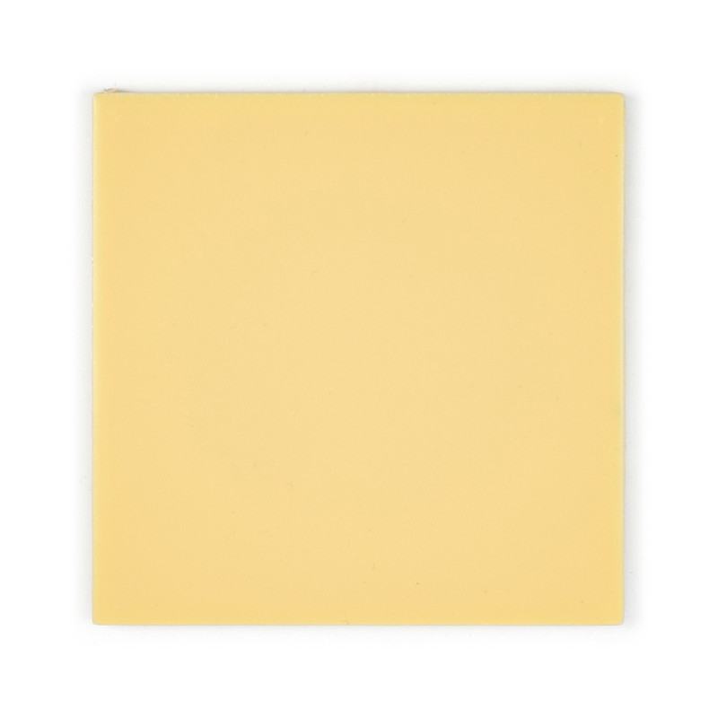 Un azulejo cuadrado liso de color amarillo claro se asienta sobre un fondo blanco, enfatizando su superficie lisa y uniforme y s