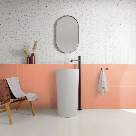 Un lavabo alto, cilíndrico y blanco se alza con un grifo negro contra una pared de azulejos de coral, rodeado por una pared supe Un lavabo alto, cilíndrico y blanco se alza con un grifo negro contra una pared de azulejos de coral, rodeado por una pared supe