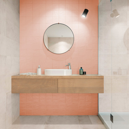 A circular mirror hangs above a wooden vanity with a sink and toiletries against a pink-tiled wall in a modern bathroom.