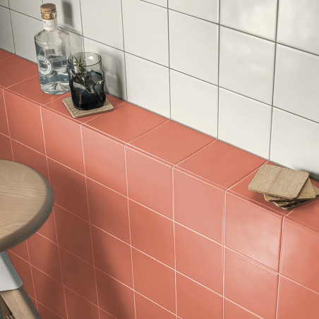 Les bouteilles et les verres reposent sur des surfaces carrelées corail et blanc dans une cuisine, avec des sous-verres à proxim