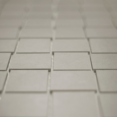 Square tiles are arranged in a staggered grid pattern, creating a subtle three-dimensional effect. The tiles appear to be light 