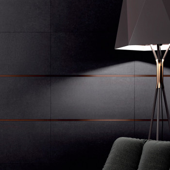 Uma luminária de chão preta ilumina uma parede escura de azulejos com finas linhas horizontais. Uma poltrona texturizada aparece