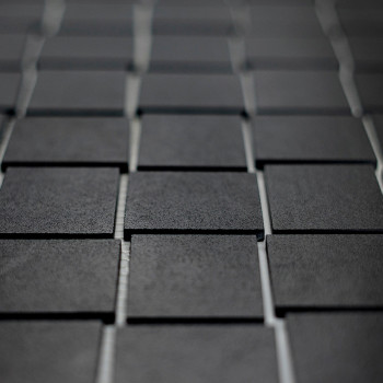 Les carreaux carrés foncés sont disposés selon un motif en grille, créant une surface texturée. Les carreaux présentent un léger