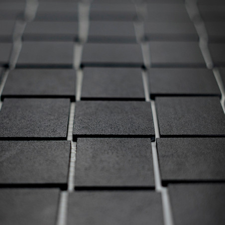 Les carreaux carrés foncés sont disposés selon un motif en grille, créant une surface texturée. Les carreaux présentent un léger