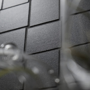 Des carreaux carrés noirs mats sont disposés selon un motif en grille sur une surface plane, avec un objet flou et clair se chev