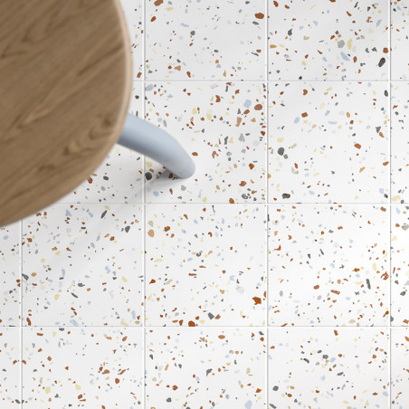Vierkante tegels met een gespikkeld patroon van veelkleurige fragmenten liggen onder een houten tafel met een lichtblauwe poot, Vierkante tegels met een gespikkeld patroon van veelkleurige fragmenten liggen onder een houten tafel met een lichtblauwe poot,