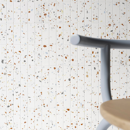 Les carreaux de terrazzo présentent des fragments colorés dispersés sur un fond blanc. Un siège en bois flou et un dossier de ch