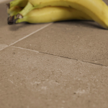Bananas rest on a smooth, light brown, square tile surface with subtle texture. The setting suggests a kitchen countertop or flo